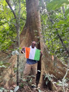 Traveler standing at the base of a large tropical tree in Banco National Park, Abidjan, holding the Ivorian flag