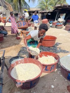 Woman preparing cassava by hand in large basins at an open-air market in Abidjan